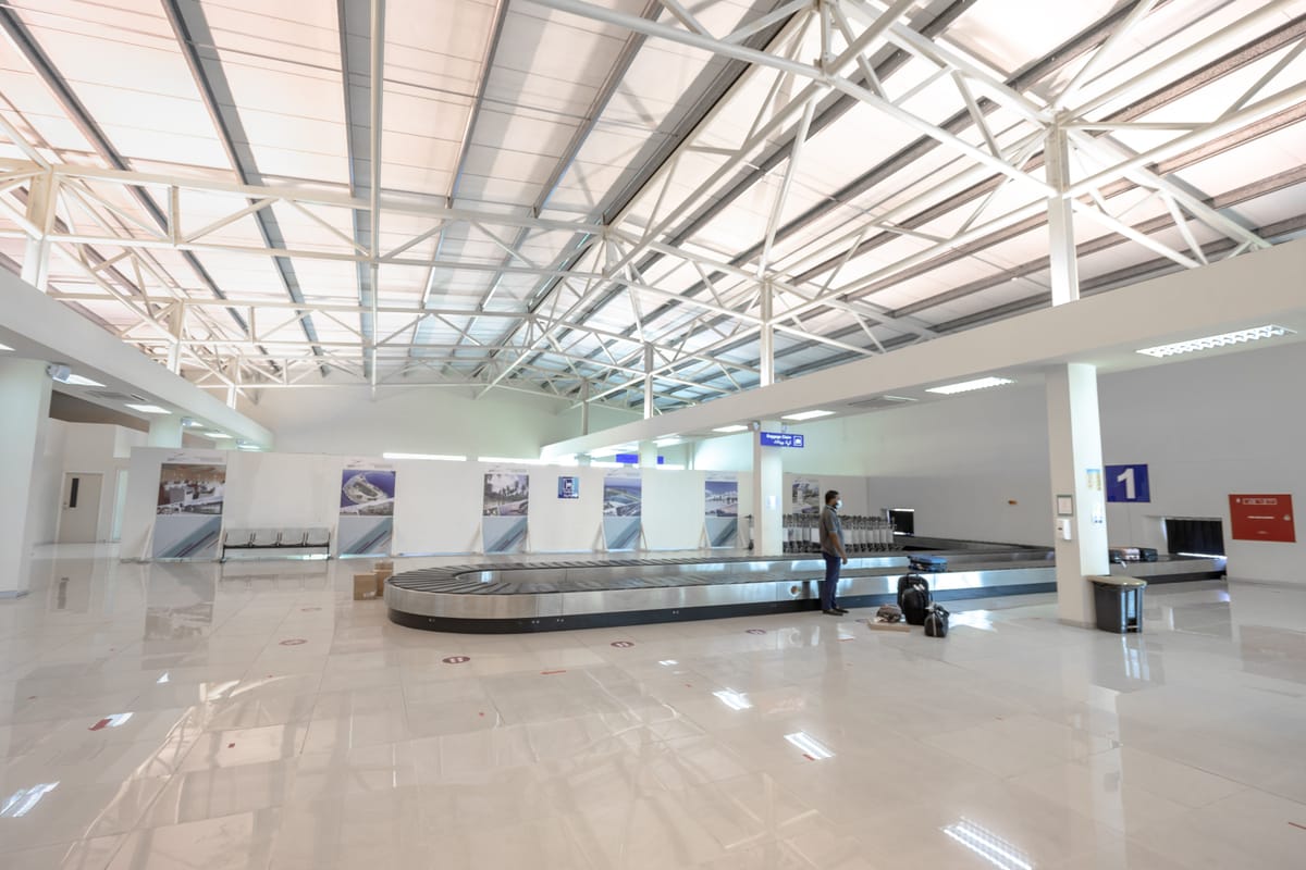 Modern airport baggage claim hall with a single traveler waiting at carousel one