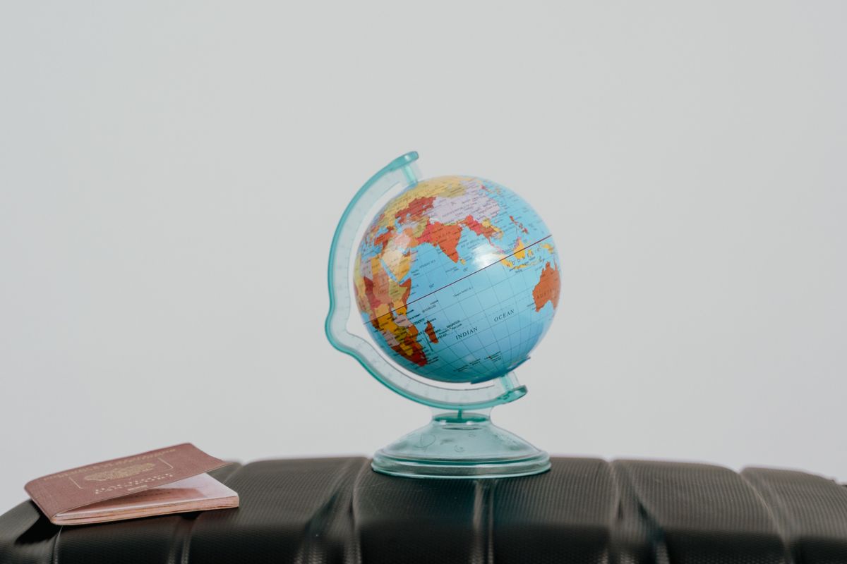 A small globe and a passport resting on a suitcase, symbolizing international travel