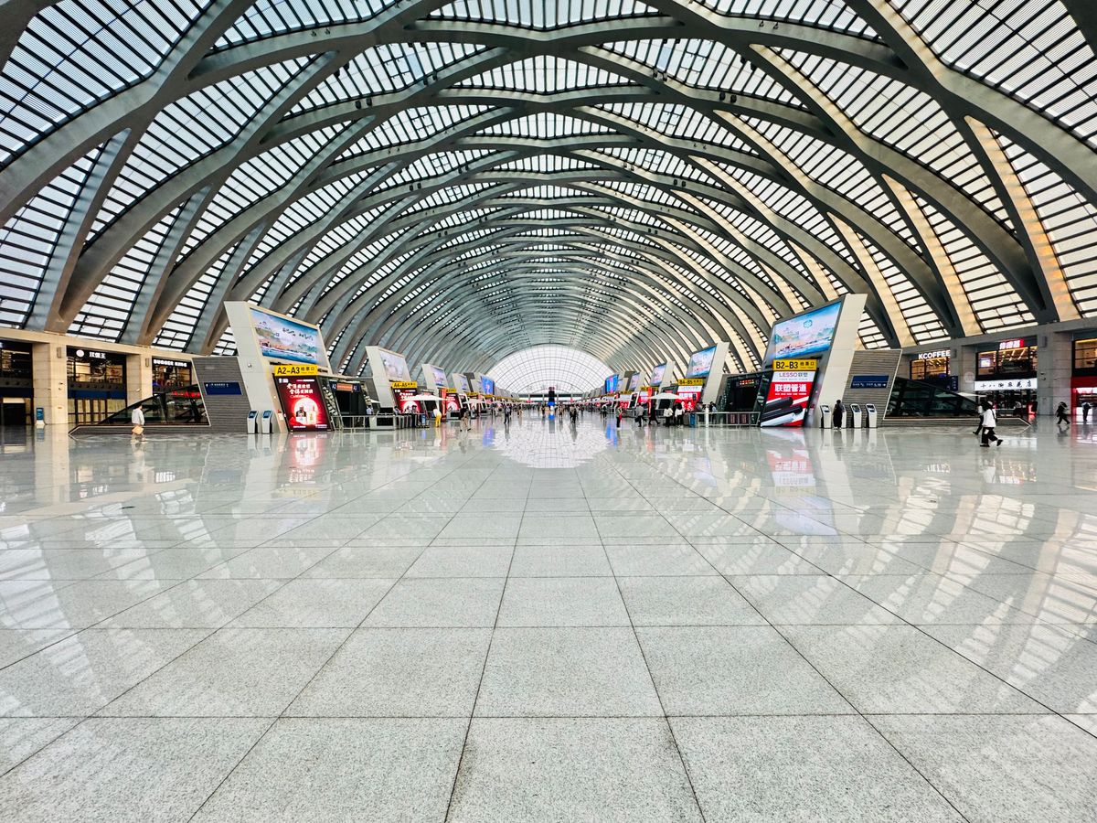 Vast modern Chinese railway station concourse with a sweeping arched glass roof