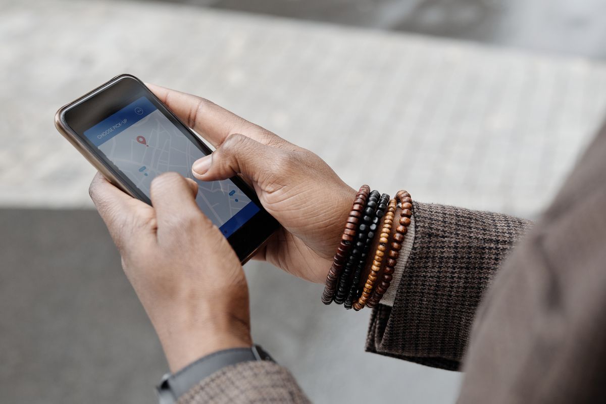 Close-up of a hand holding a smartphone showing a ride-hailing app map with a pick-up location pin