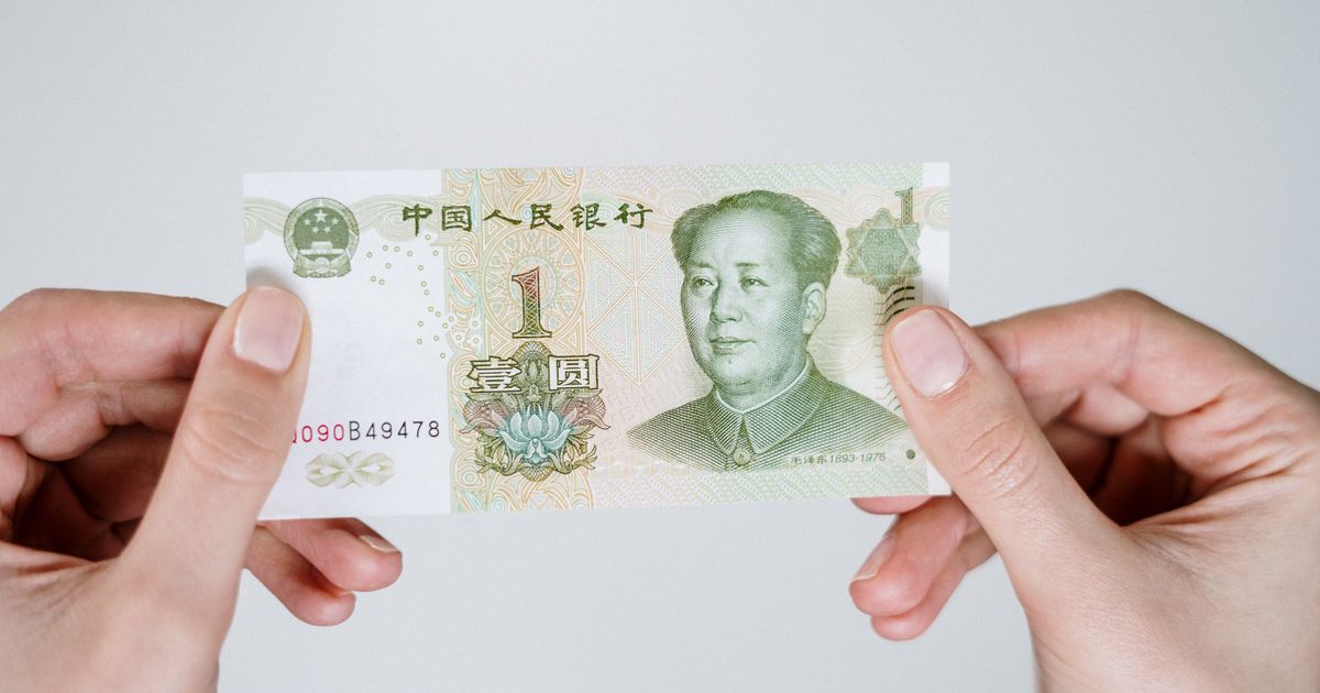 Two hands holding a Chinese one-yuan RMB banknote against a plain background