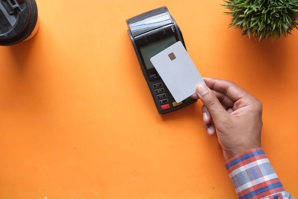 Top-down view of a hand holding a bank card over a card payment terminal on an orange desk