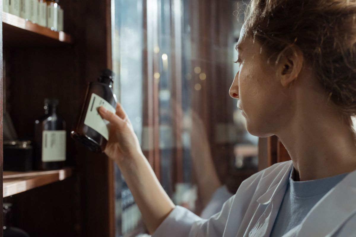 A pharmacist in a white coat selecting a labeled medicine bottle from a wooden pharmacy shelf
