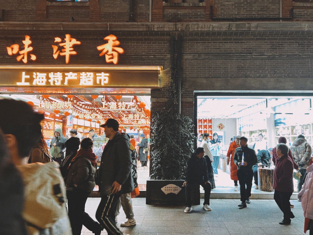 Busy Shanghai shopping street at night with large Chinese-character shop signs glowing above pedestrians
