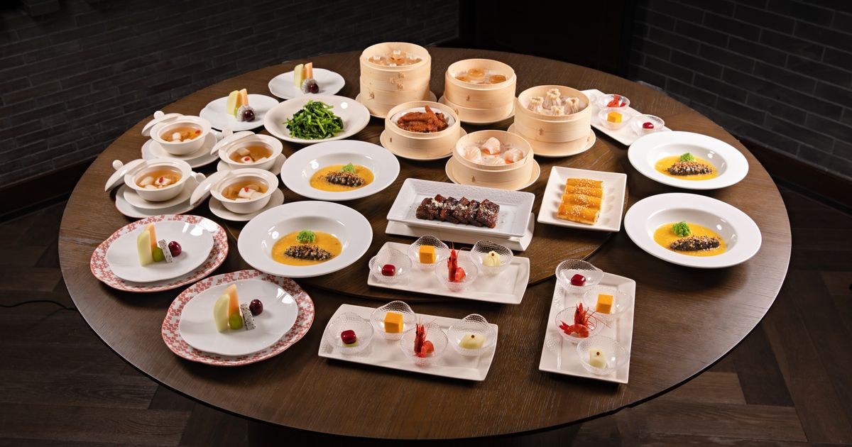 A round restaurant table set family-style with many shared Chinese dishes and bamboo steamers of dim sum
