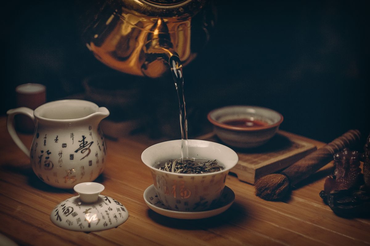Tea being poured into a lidded gaiwan cup beside a pitcher decorated with Chinese calligraphy