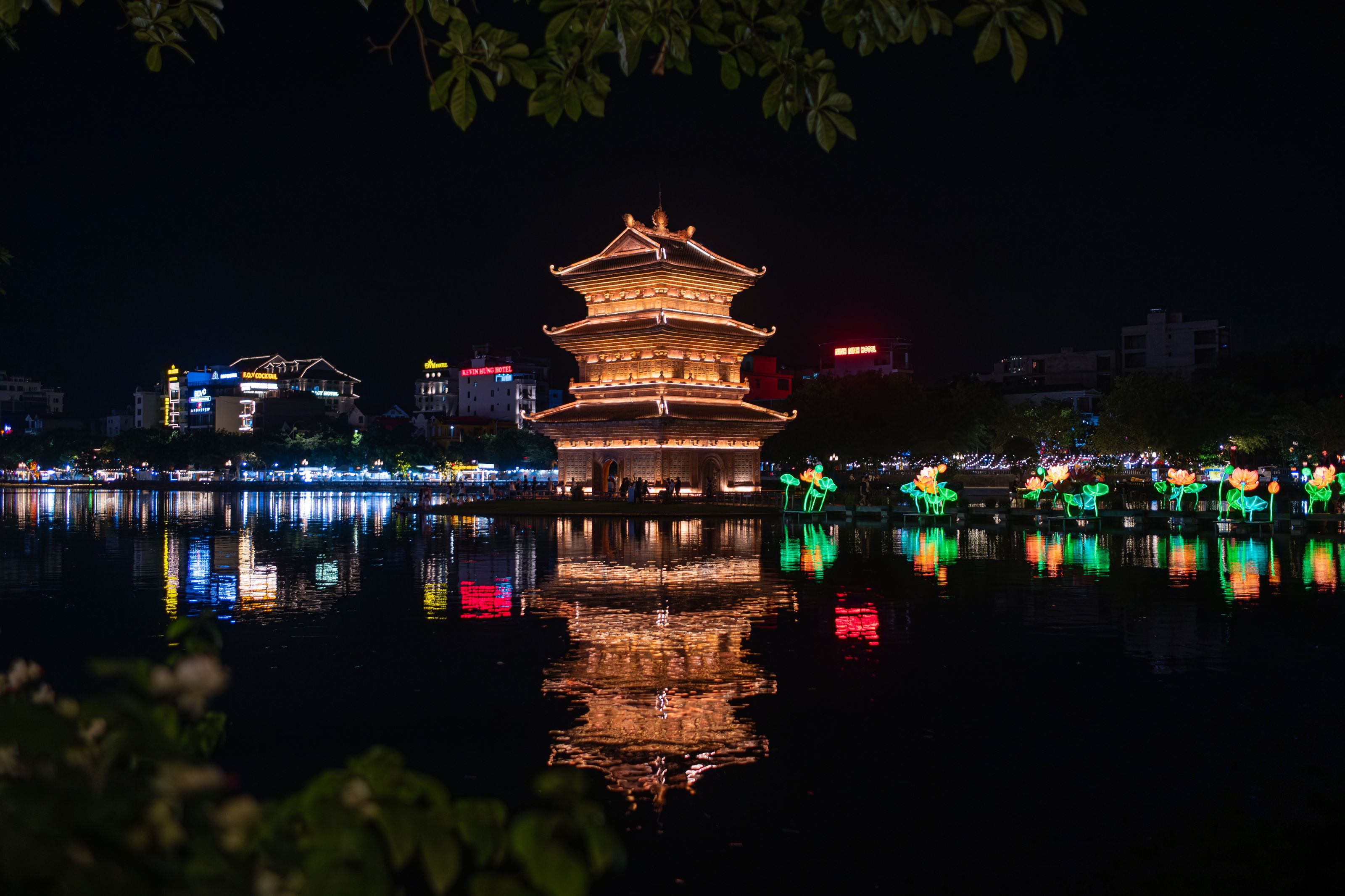 A floodlit pavilion and lotus lanterns mirrored in the lakes during the night cruise