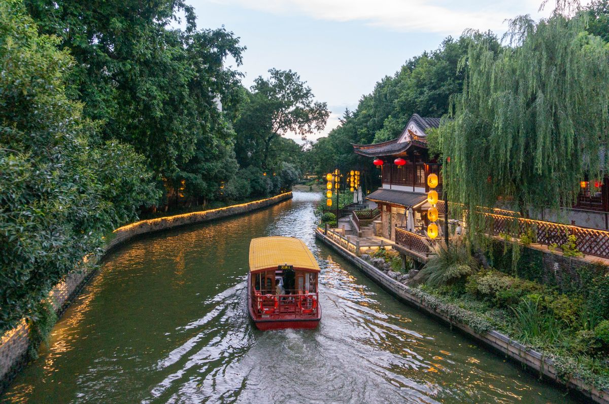 A traditional canal boat passing lantern-lit banks at dusk
