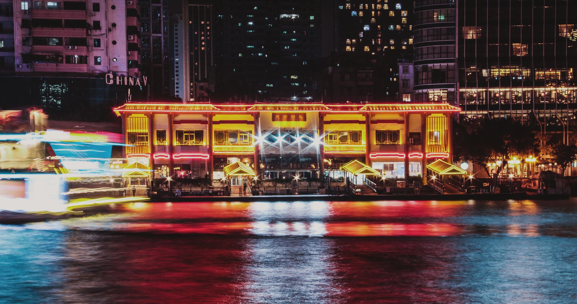 A brightly lit riverside hall on the Pearl River with light trails from a passing cruise boat