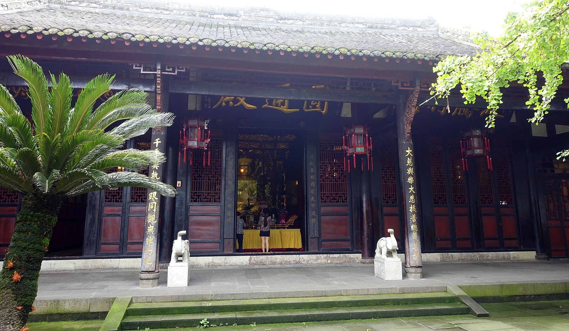 Hall of Wenshu Monastery framed by palms and stone lions