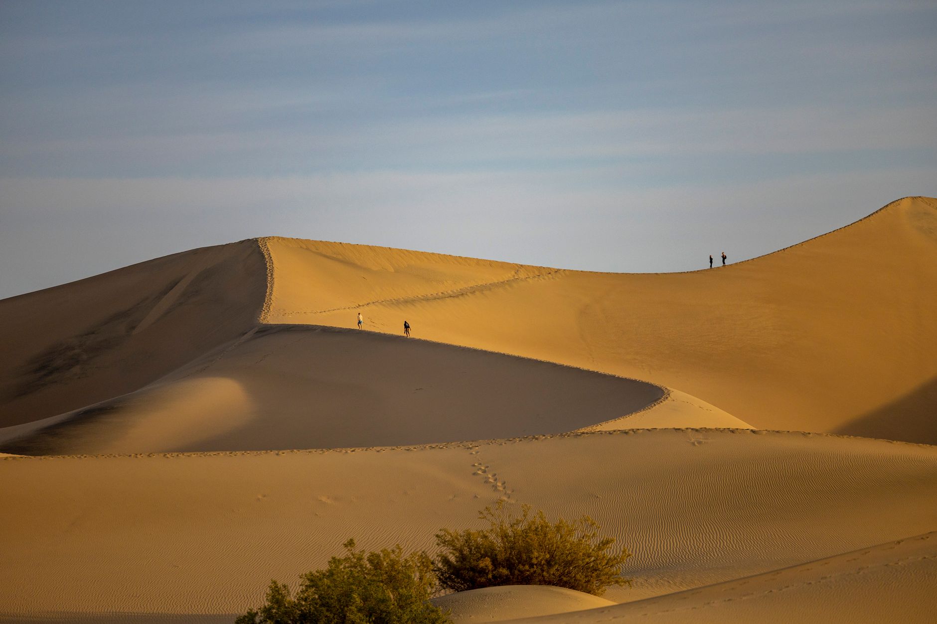Visitors climbing the singing sand dunes at sunset