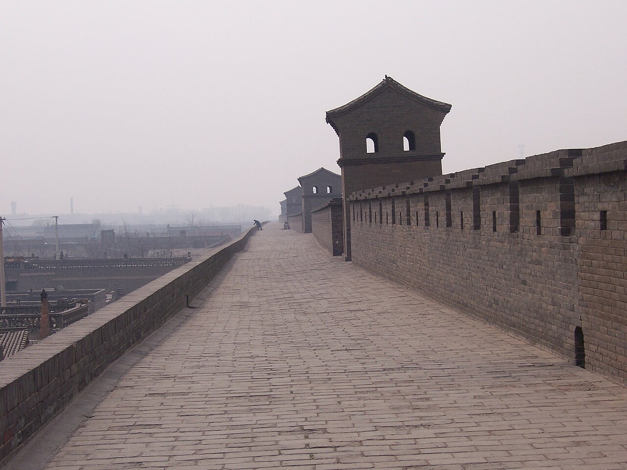 Visitors strolling the broad paved walkway on top of the Pingyao wall beside a watchtower