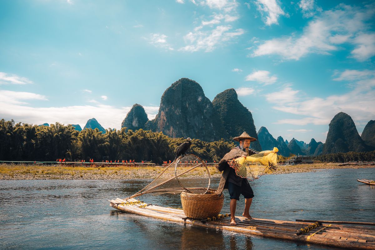 Tourists on a bamboo raft poled along the green Yulong River